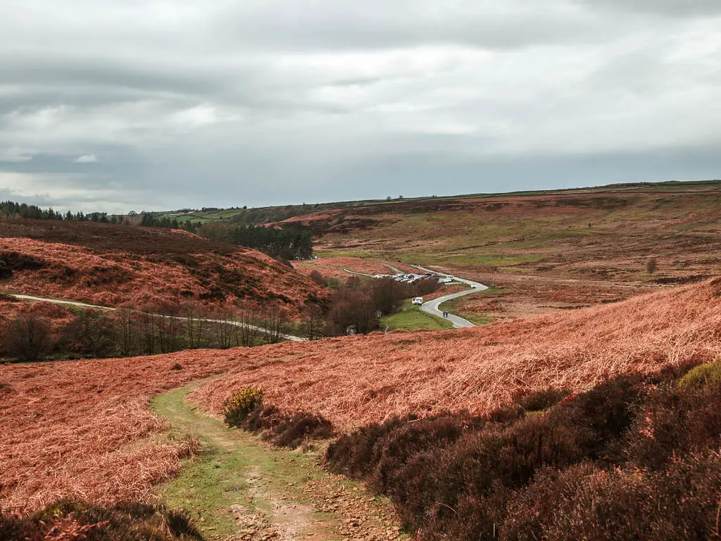 A grass trail winding downhill, with a view to the road through the valley at the bottom.