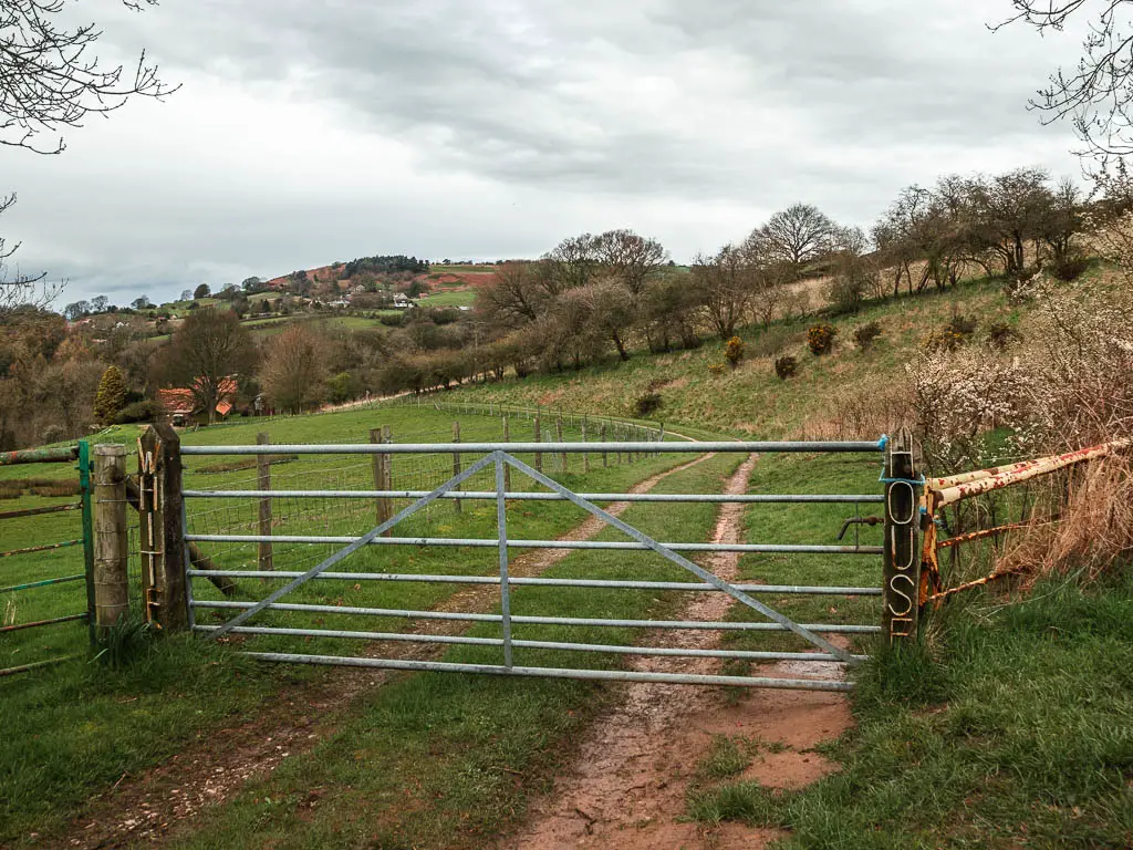 A metal gate leading towards a dirt track and fields. On the wooden post next to the gate it says 'White' "House'.