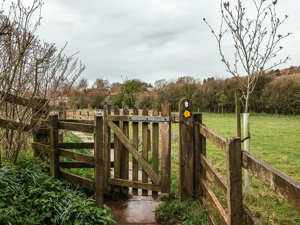 A small wooden gate with a yellow arrow sign on it, pointing straight ahead.