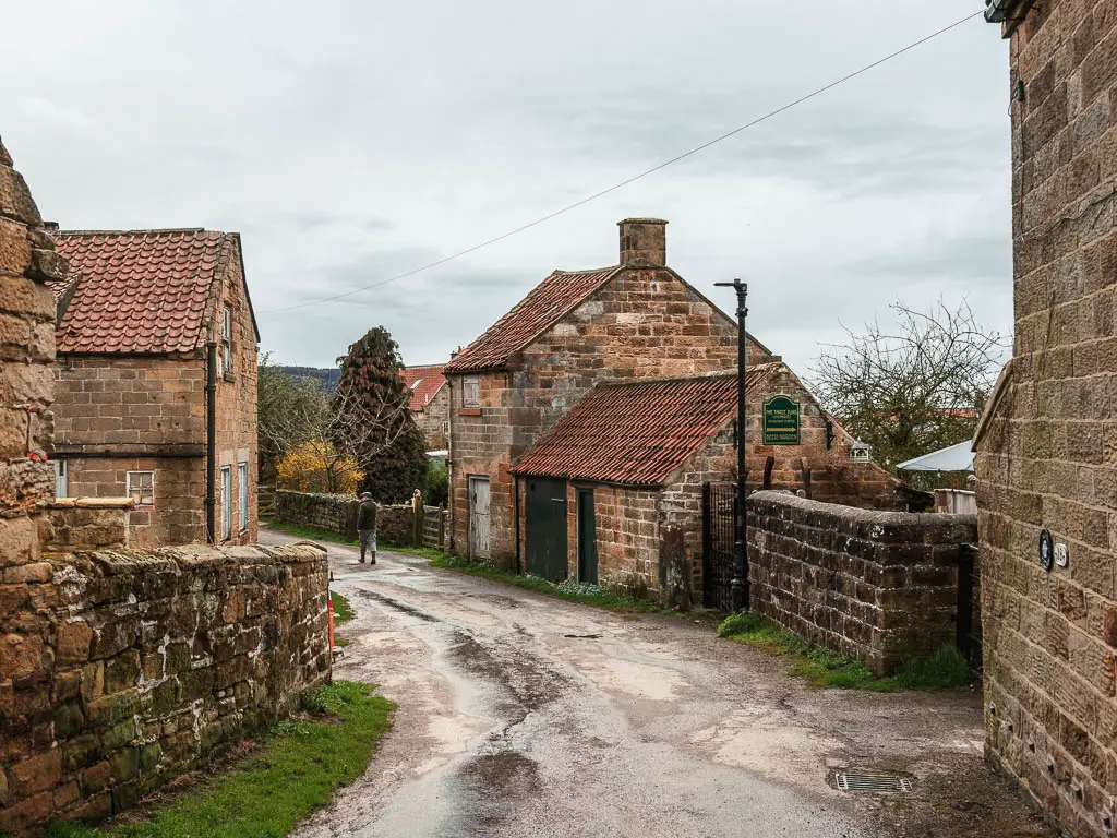 A road lined with stone walls and stone cottages on the walk back into  Osmotherley. there is a person walking on the road ahead. 