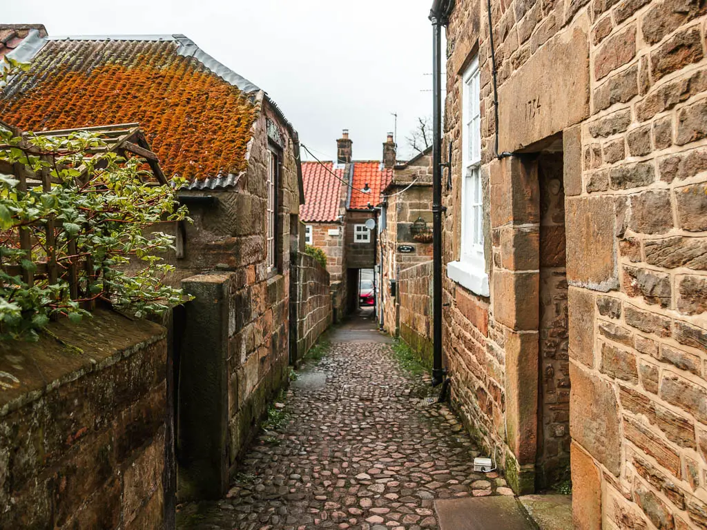 A cobbled alley through the stone walled houses, and a gap inder the house straight ahead, at the end of the Osmotherley walk route.