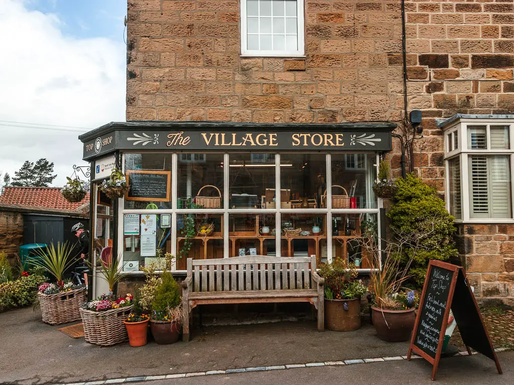 The village store in Osmotherley, with a wooden bench and lots of flower pots outside. 