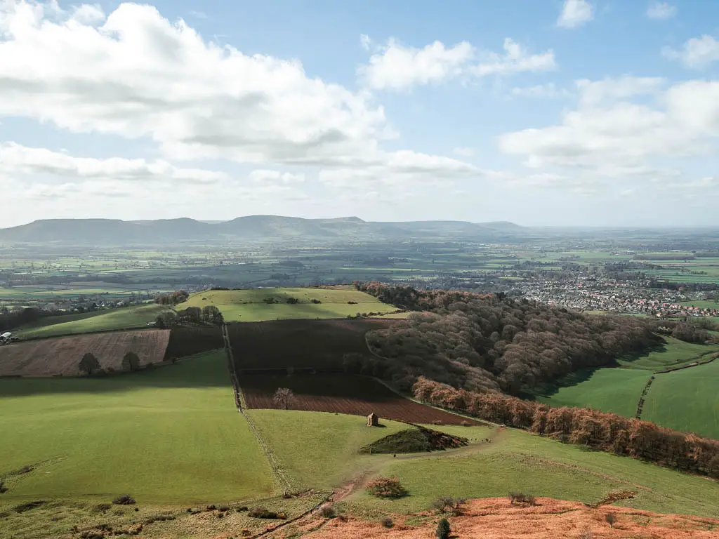 Looking down to the undulating patchwork green and brown fields as far as the eye can see, to some peaks in the distance, after the walk to the top of Roseberry Topping.
