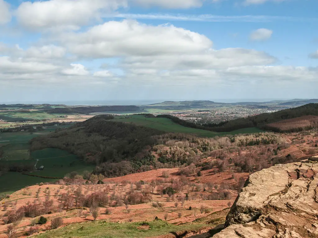 Looking down across the undulating fields of grass and trees as far as the eye can sea. In shades of green, orange and brown.
