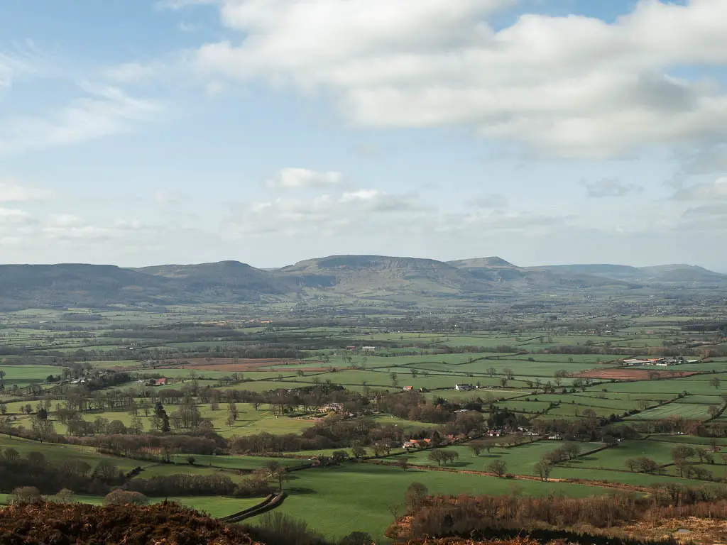 Looking down and across the valley of green grass fields all the way to some hills in the distance, in the North York Moors.