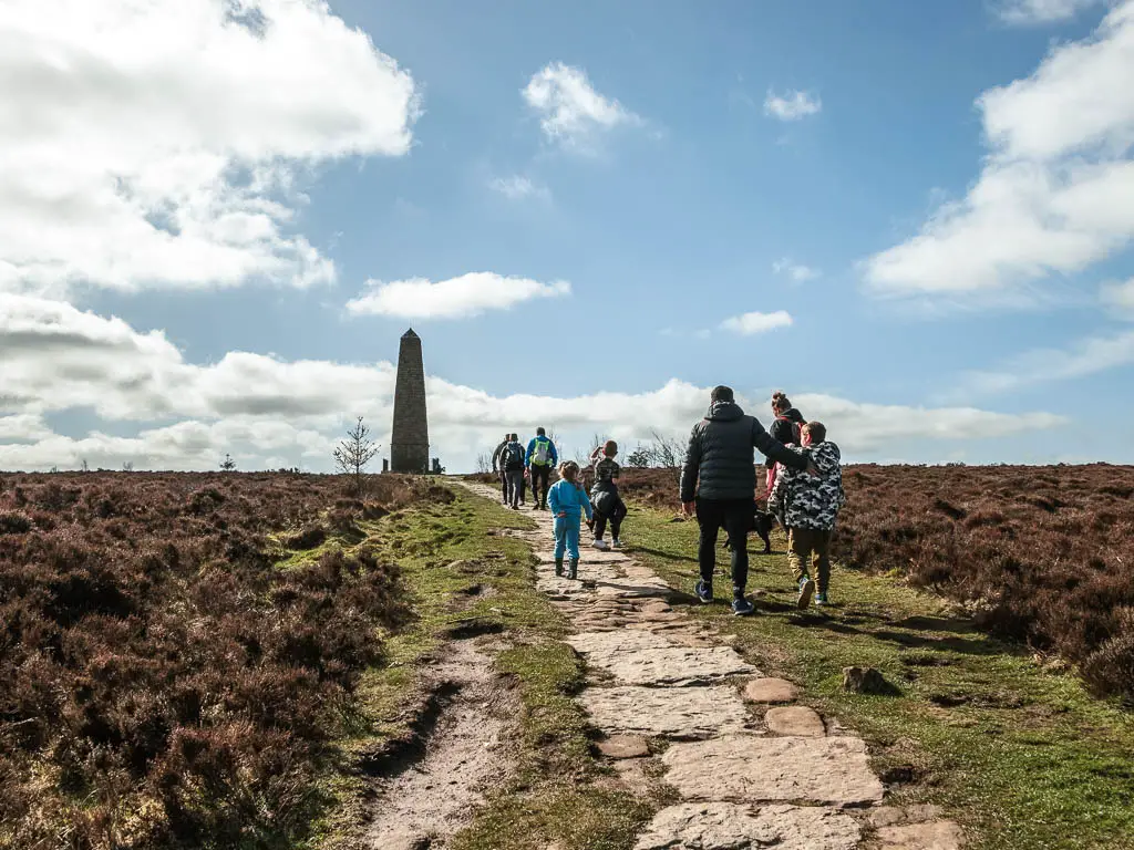 A paved path leading ahead to the Captain Cook's Monument, with lots of people walking on the path.