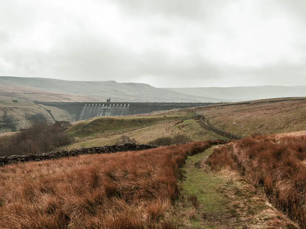 A grass trail through the tall grass, with a view to the Angram Dam ahead.