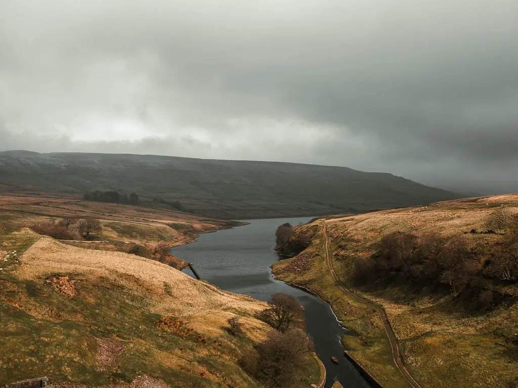 Looking across the Scar House Reservoir, surrounded by the undulating moors of Nidderdale, on the walk around it. It is a grey gloomy day.