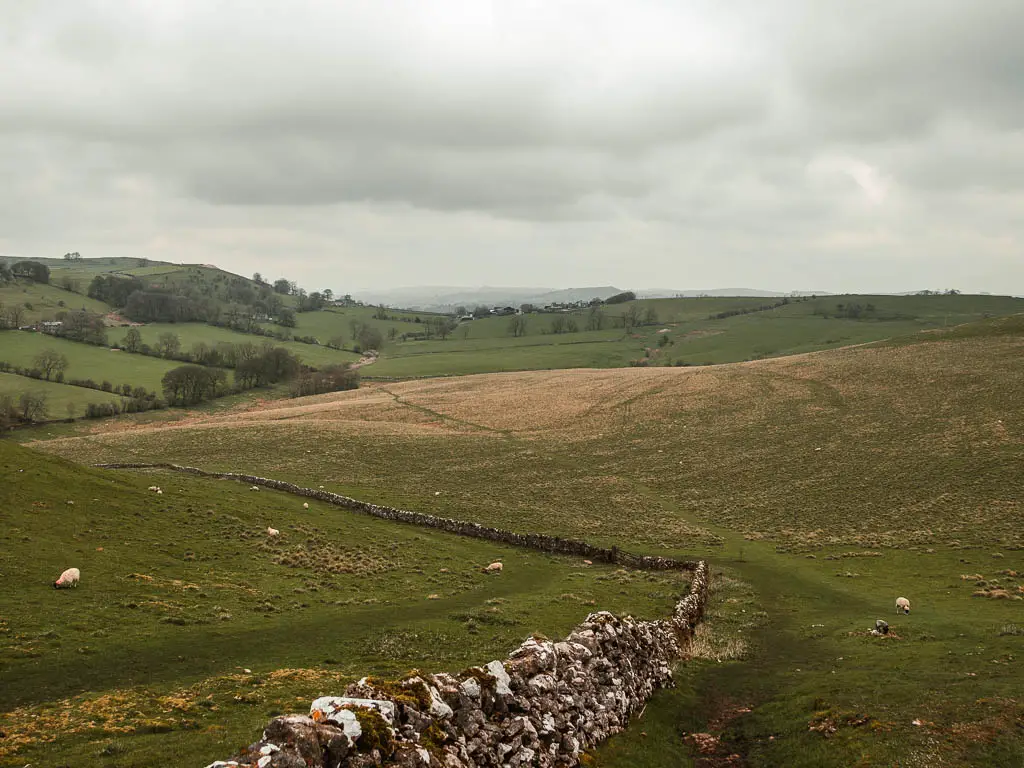 Looking down along the stone wall, and across the undulating fields of green into the distance. 