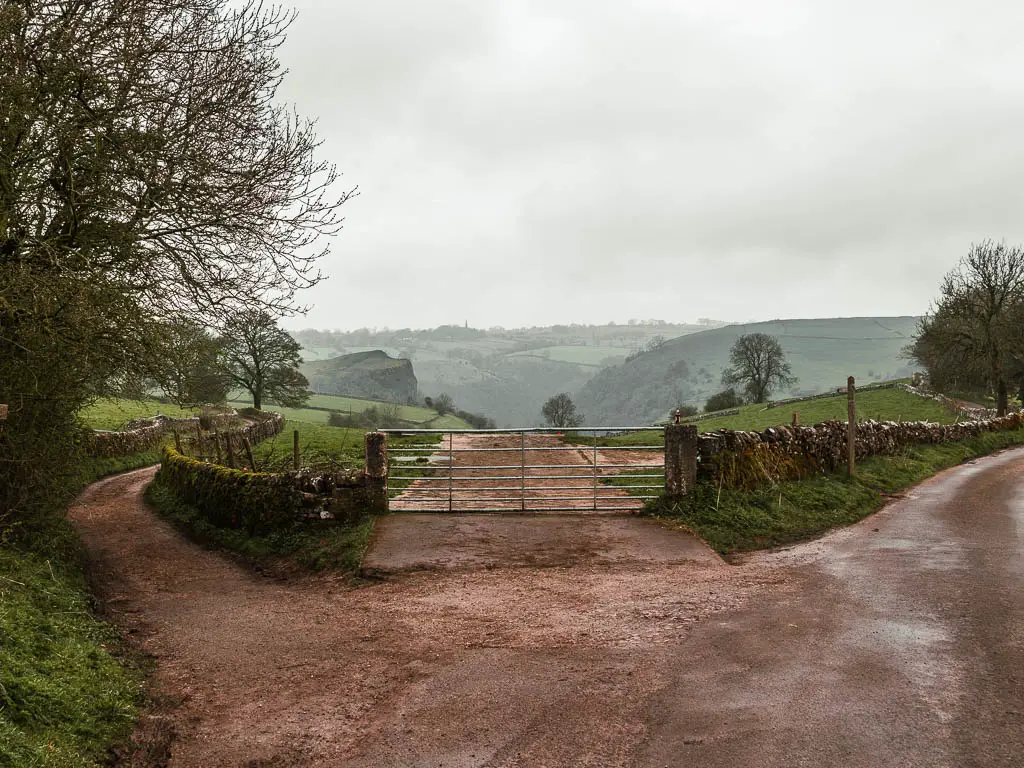 A junction, with the road to the right, a metal gate straight ahead, and a path to the left, at the start of the walk to Thor's Cave.