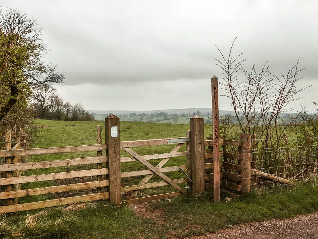 A wooden gate and fence leading into a large grass field.