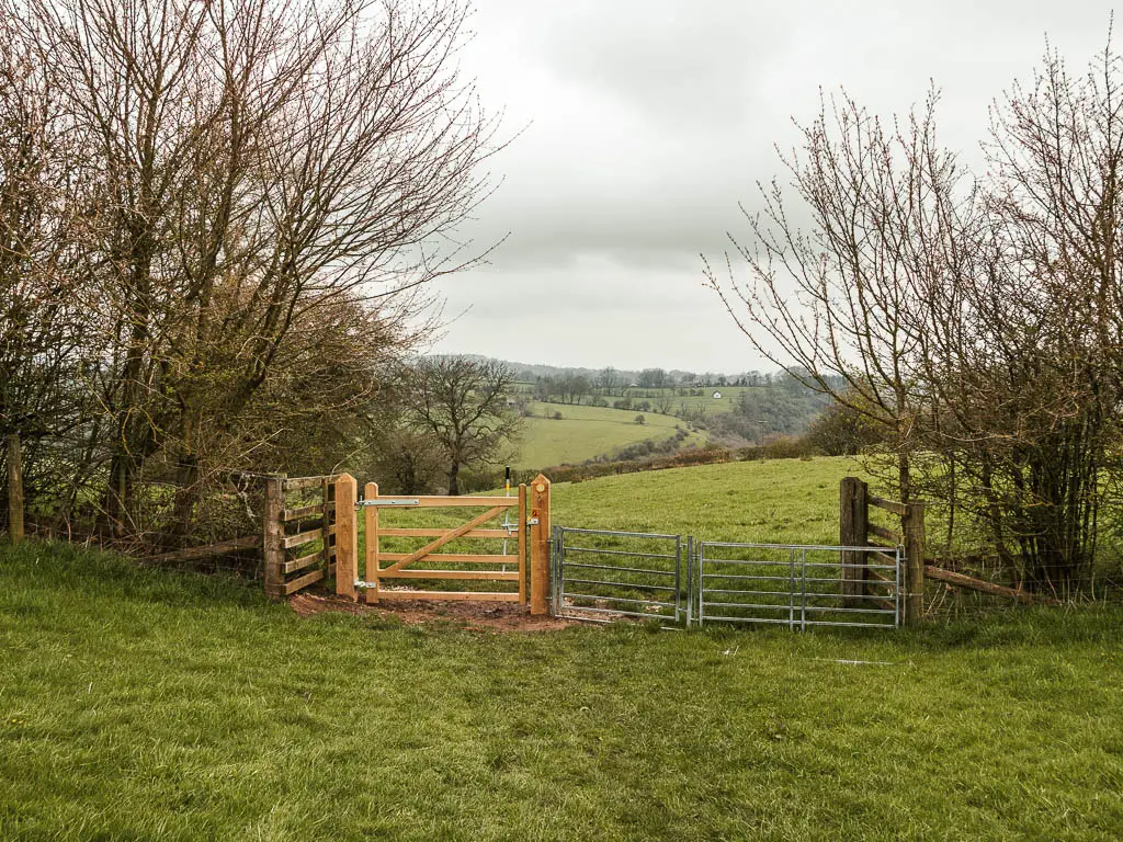 A wooden and metal gate leading into a large grass field. 