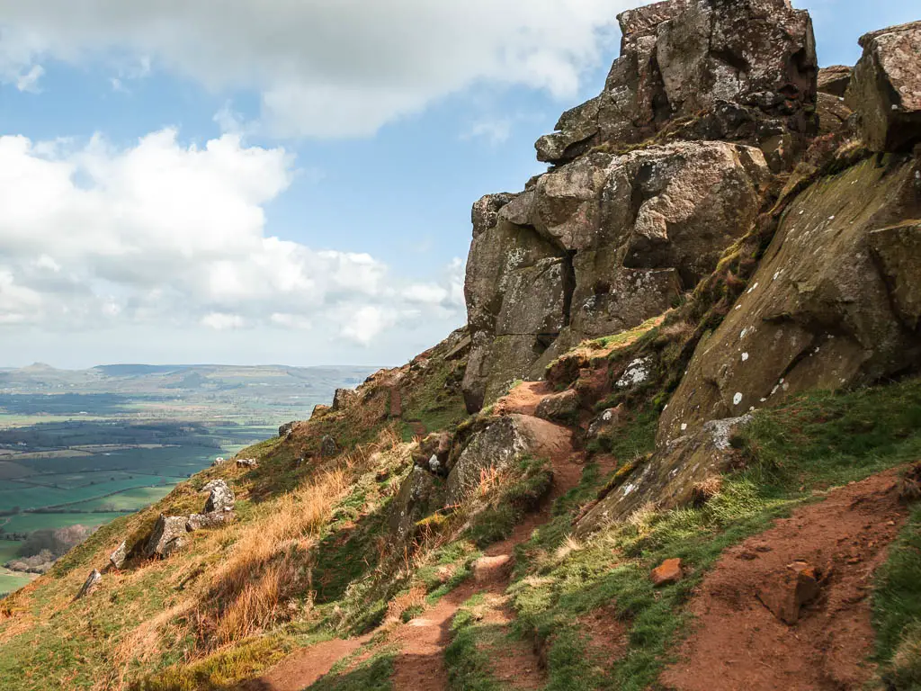 The rocks of the Wainstones rising up on the right, with a trail on the left on the walk around them. There is a steep drop down to the left.