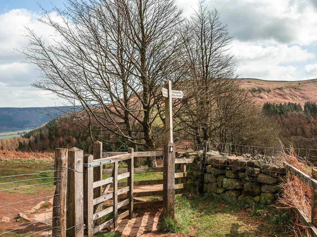 A wooden gate and stone wall, with a wooden trail signpost. 