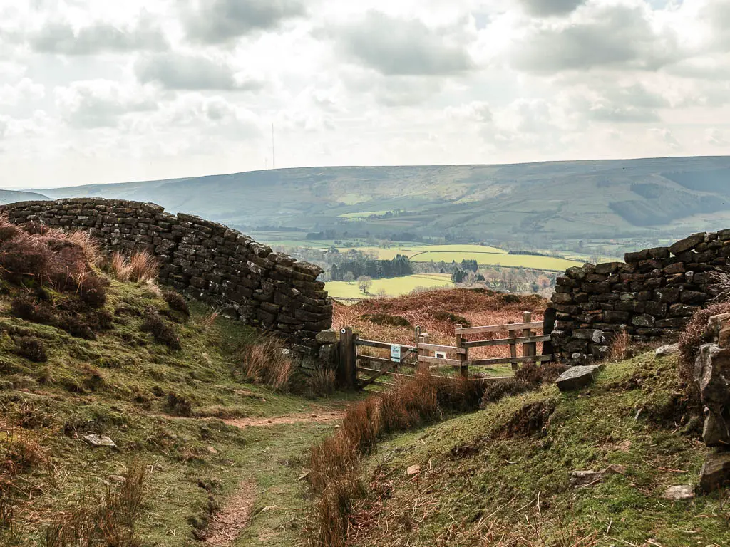 A trail leading through the middle of the hills to a wooden fence in the stone wall.