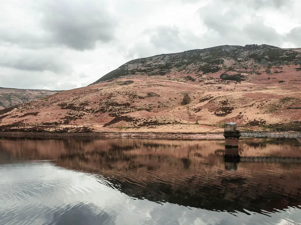 Looking across Yeoman Hey reservoir, with a moorland hill rising up on the other side, casting a shadow down on the water.