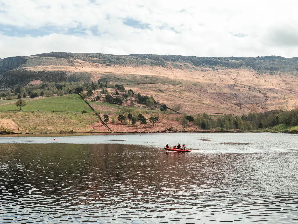 A small dingy boat on the water, with a big moorland hills on the other side.