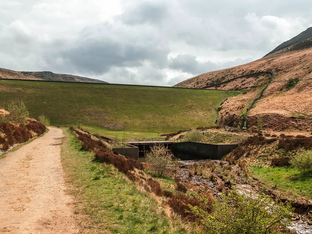 A dirt path on the left and a big green grass hill rising up ahead.