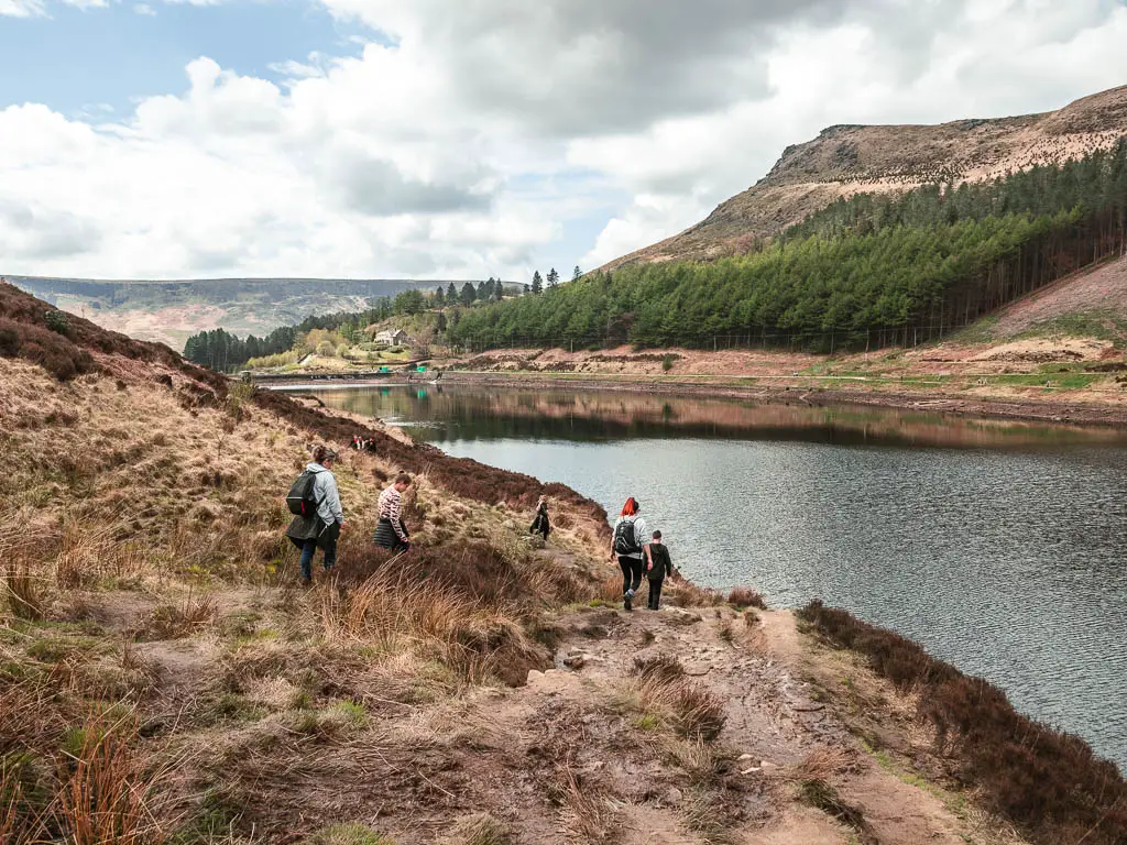 A group of people walking down the rugged ground towards the reservoir on the right, on the walk back towards Dovestone.