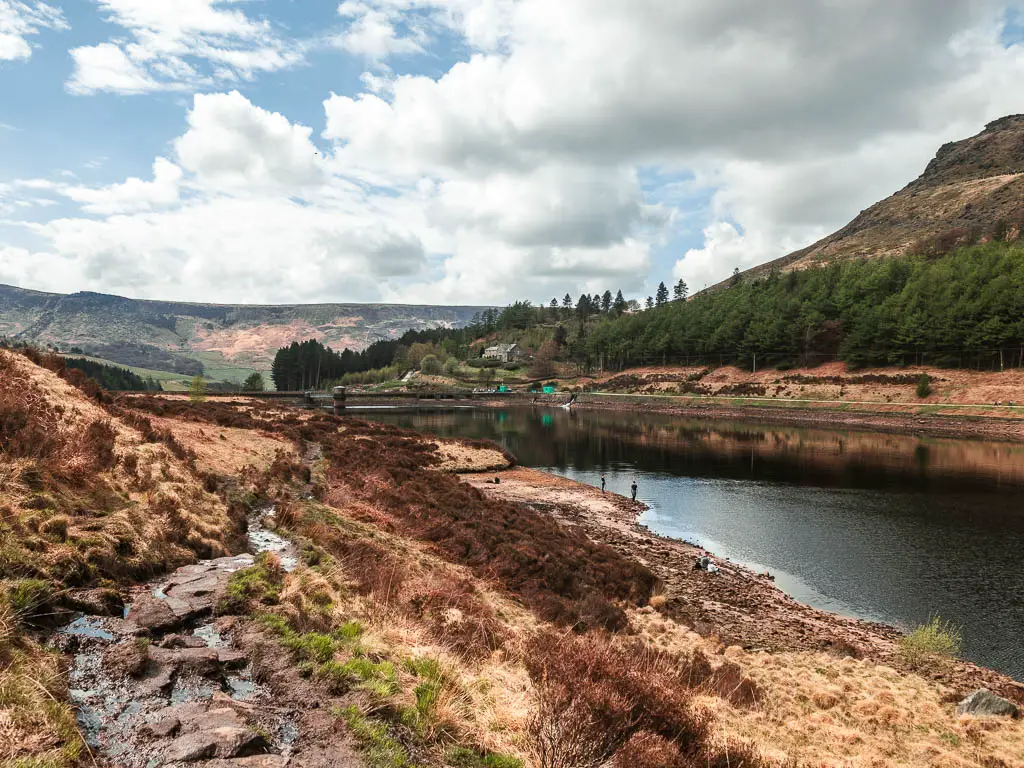 A wet, muddy rocky trail on the left with the water below to the right, on the walk back towards Dovestone Reservoir.