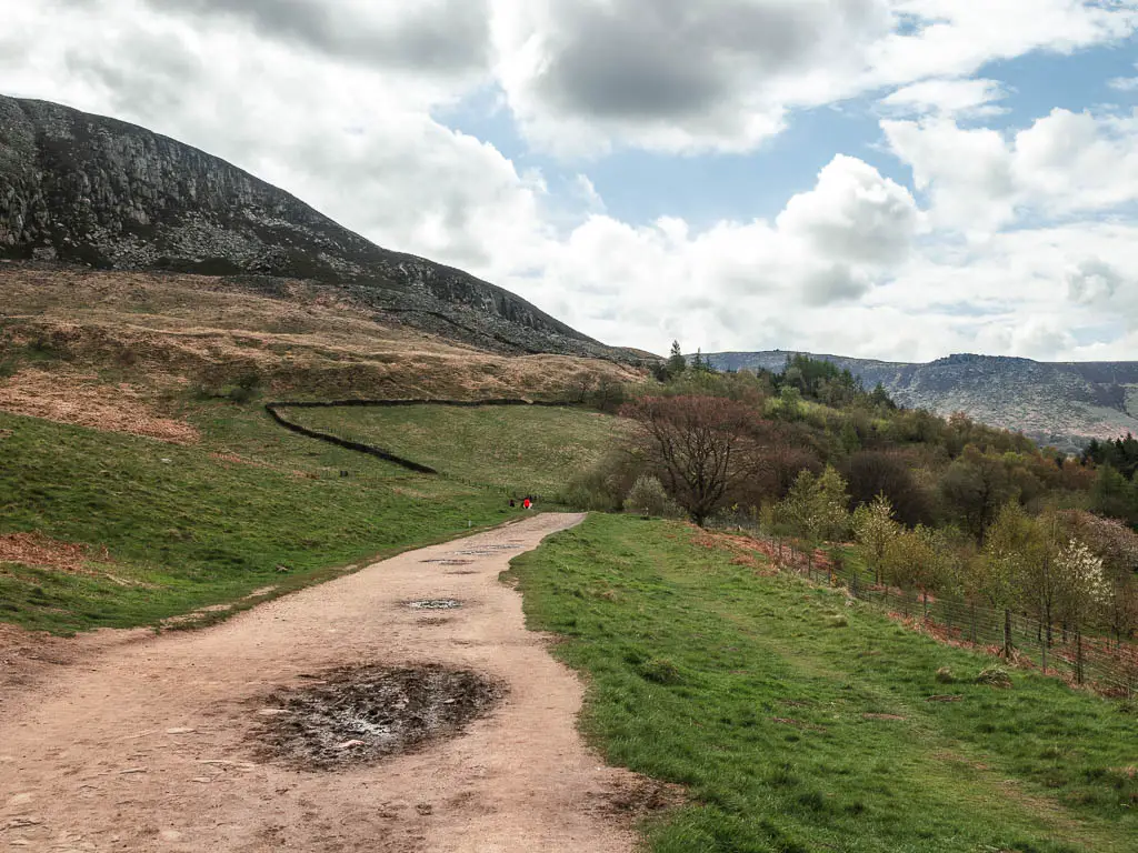 A dirt path with a grass hill leading up to the left and grass bank to the right.