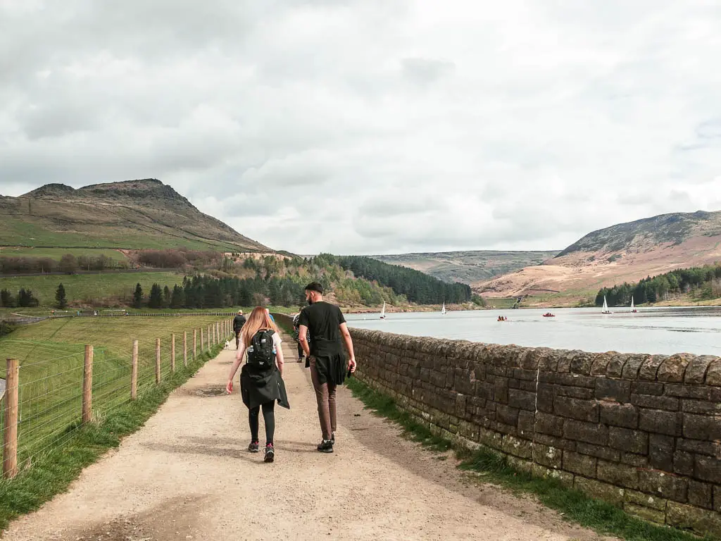 Two people walking along the path with a stone wall and dovestone reservoir to the right. There are hills in the distance.