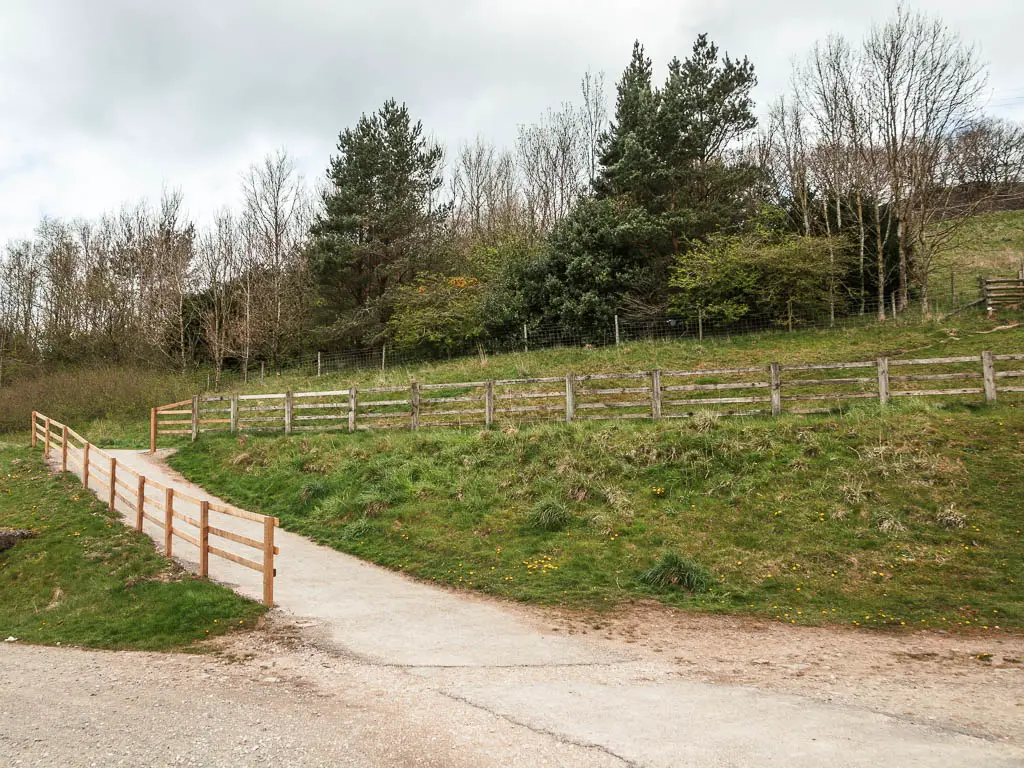 A path leading left up a small hill, lined with a wooden fence to the left and then the right.
