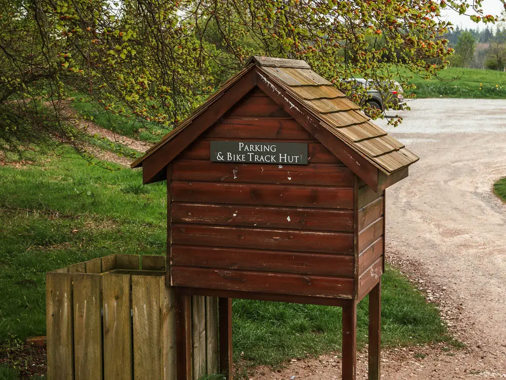 A small wooden A frame hut on stilts, with a sign that says 'Parking and Bike track hut'.