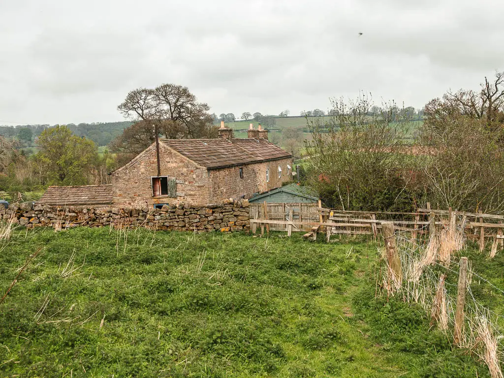 A small grassy area, with a stone wall ahead, and farm building on the other side.