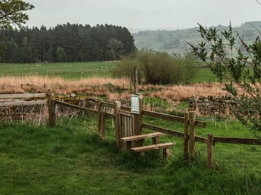 A stile in a wooden fence, separating the grass fields.