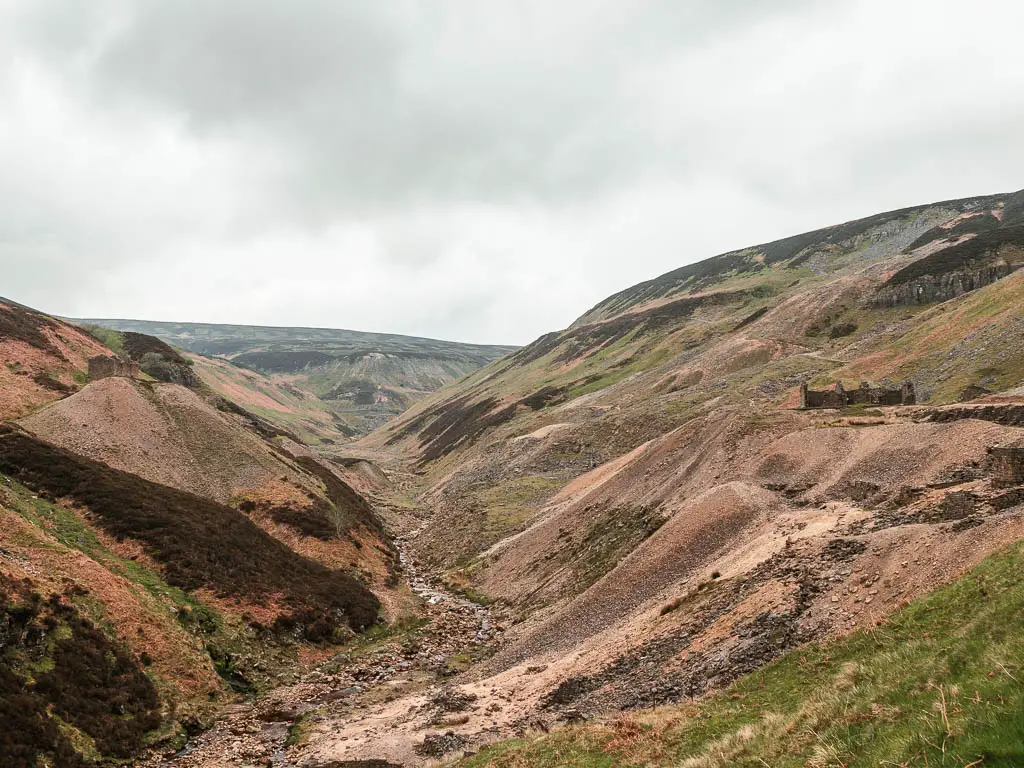 Looking down through the valley of brown coloured moorland hills on the walk through Gunnerside Gill. There are mine ruins in the distance on the right side of the hill.