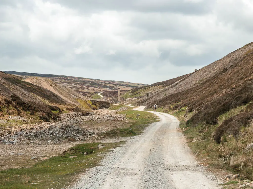 A grey road winding ahead through the valley. There is a person walking on the trial ahead.