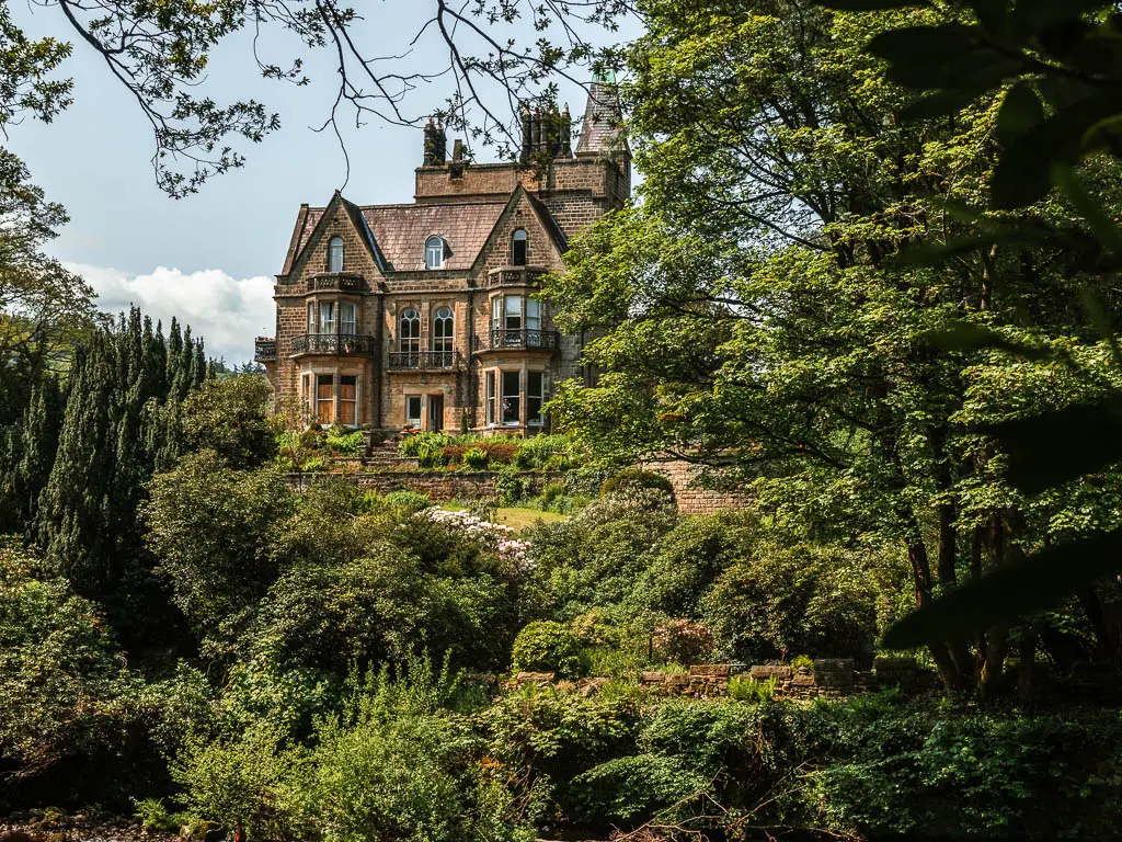 A big Manor House on the other side of the river, surround by green bushes and trees, on the walk from  Pateley Bridge.