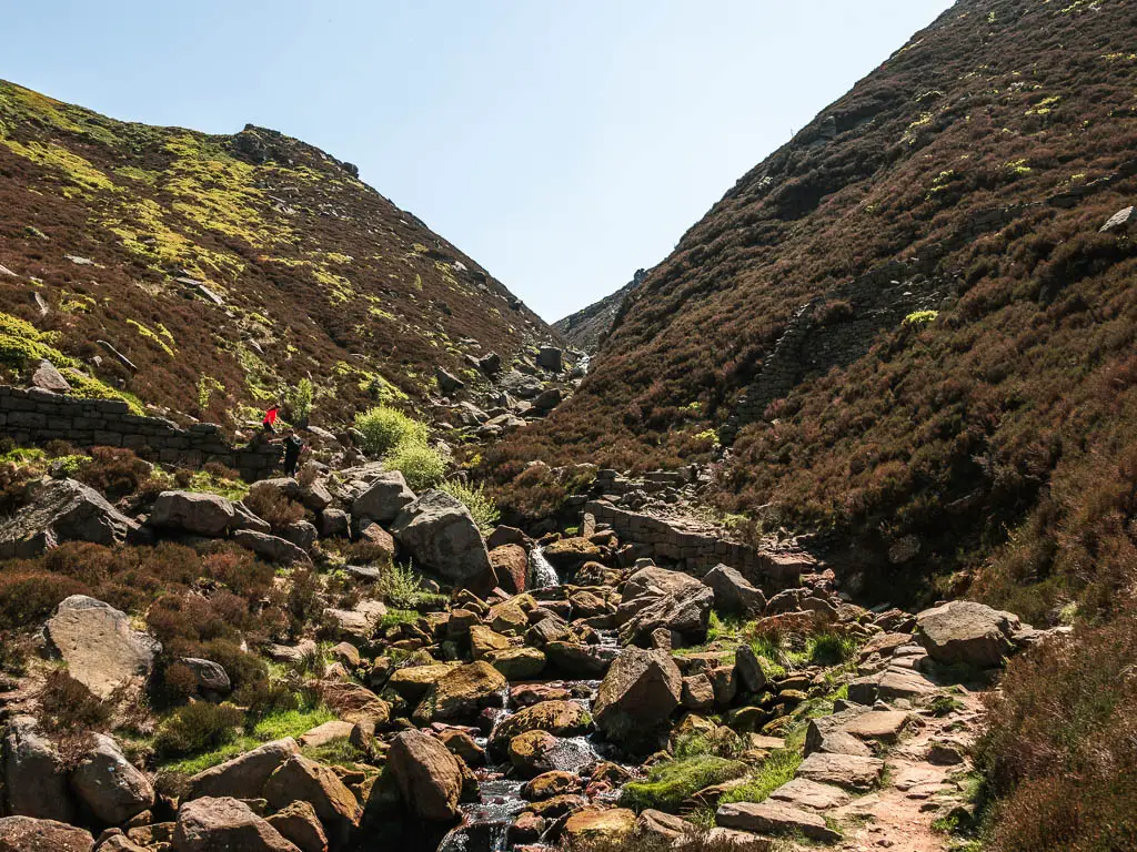 A mass of rocks leading up through the middle of a narrow valley, with a small dirt trial on the right, on the walk up towards the Trinnacle.