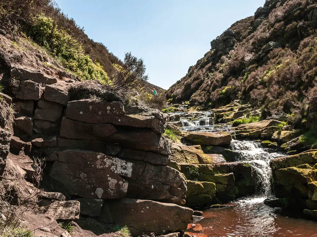 Looking up along the rocky valley, with a river and waterfall flowing down it, on the hike up to the Trinnacle.