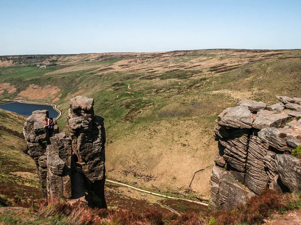 The big Trinnacle rock standing high above the valley on the walk along the trail around it in the Peak District. The blue reservoir is at the bottom of the valley on the left.