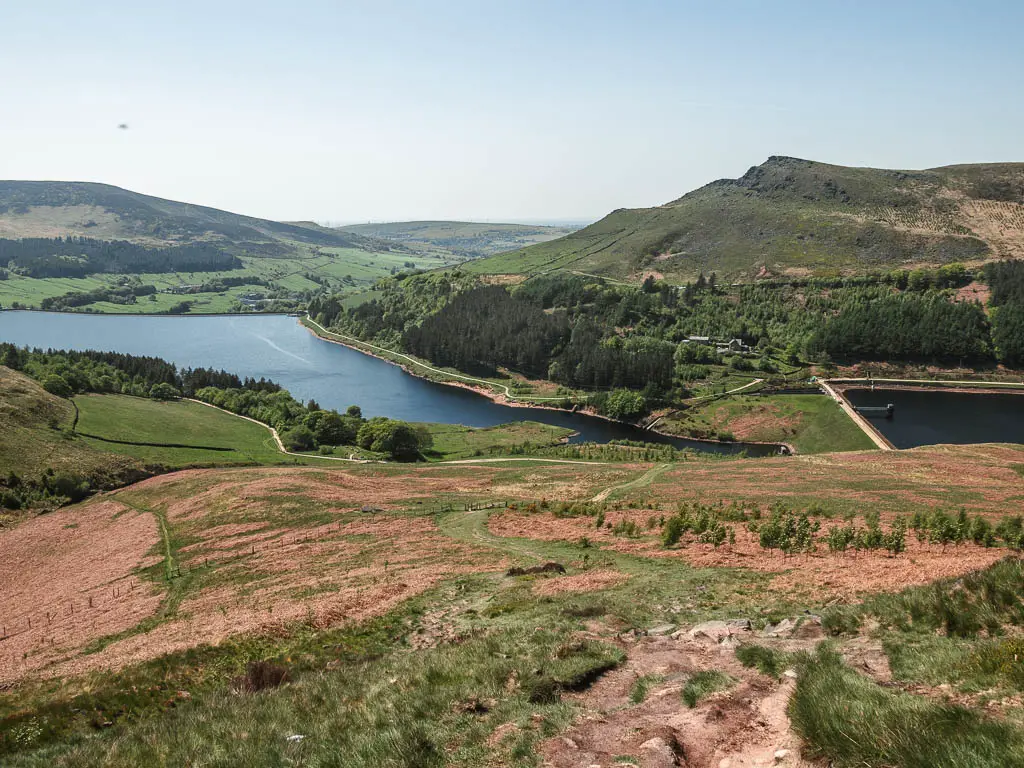 A dirt trail leading down the grass hillside, near the end of the Trinnacle circular walk. The trial leads down to the reservoir at the bottom of the valley, with hills rising up on the other side.