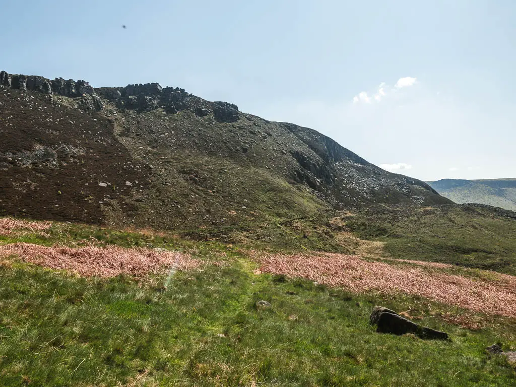 A very thin grass trail leading towards a big hill ahead.