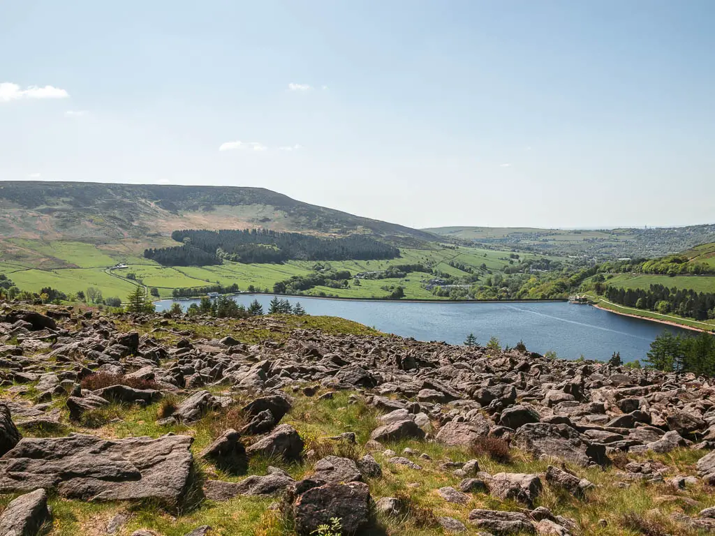 Looking across a mass of rocks on the rugged grass hillside, near the end of the Trinnacle circular walk. The blue reservoir is at the bottom of the hill.