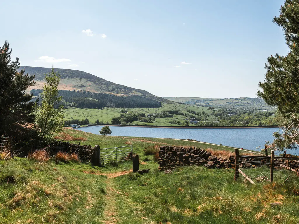 The grass trial leading down to a metal gate in the stone wall, and the reservoir further down at the bottom of the hill.