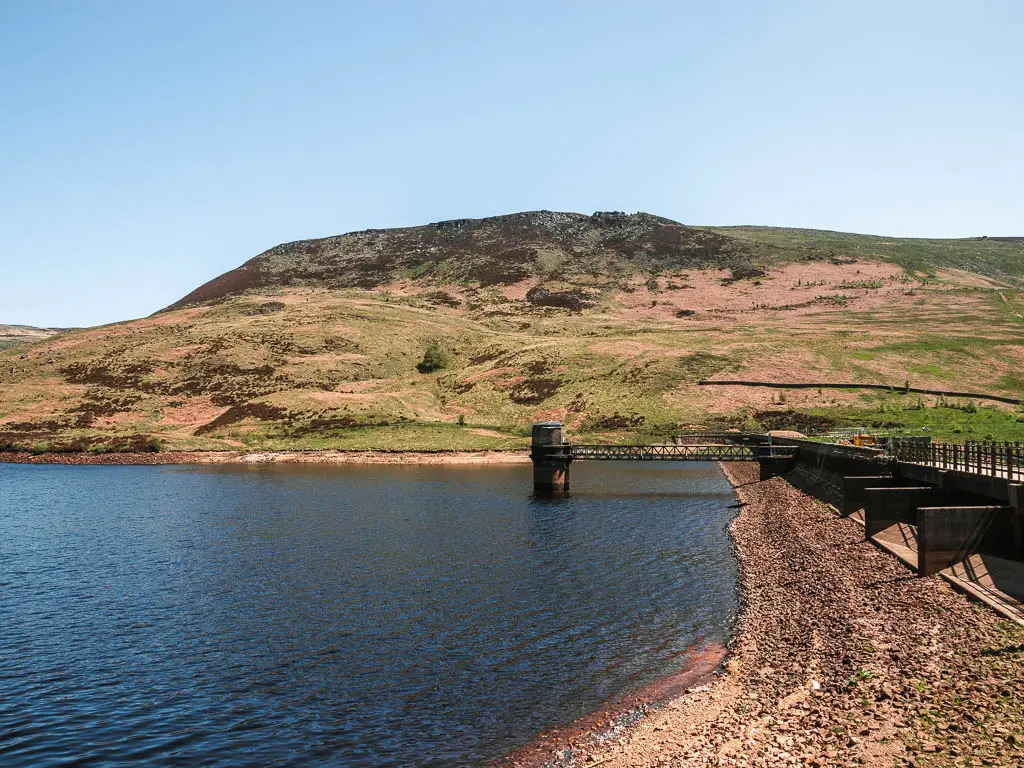 Looking along the edge of the Yeoman Hay Reservoir, with a rocky bank on the right, and the hills rising up on the other side.