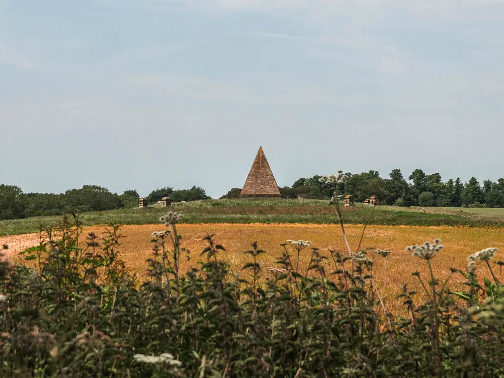 A pyramid on top of a hill, on the walk towards Castle Howard. The field is an orange colour, then turns to green at the top.