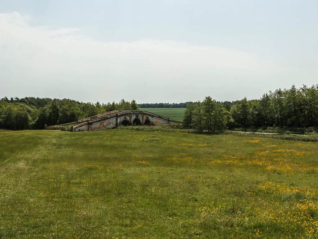 Looking across the grass field towards an ornate bridge.