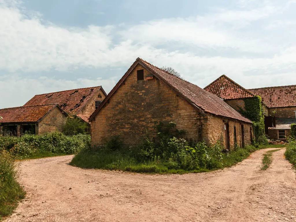 A group of stone walled houses and sheds, with the dirt path running around them.