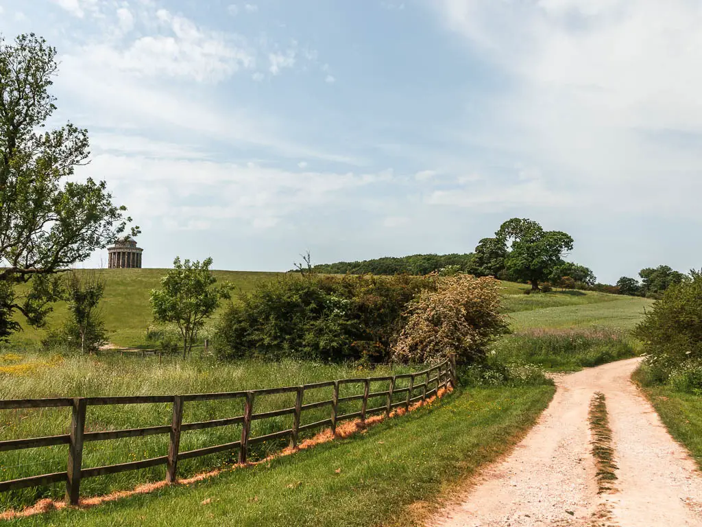 A path on the right, and fields with small trees and bushes to the left. The Castle Howard Mausoleum is visible in the distance to the left, on to of a hill.
