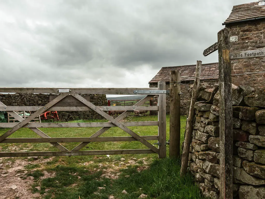 A wooden gate with part of the stone walled farmhouse visible to the right.