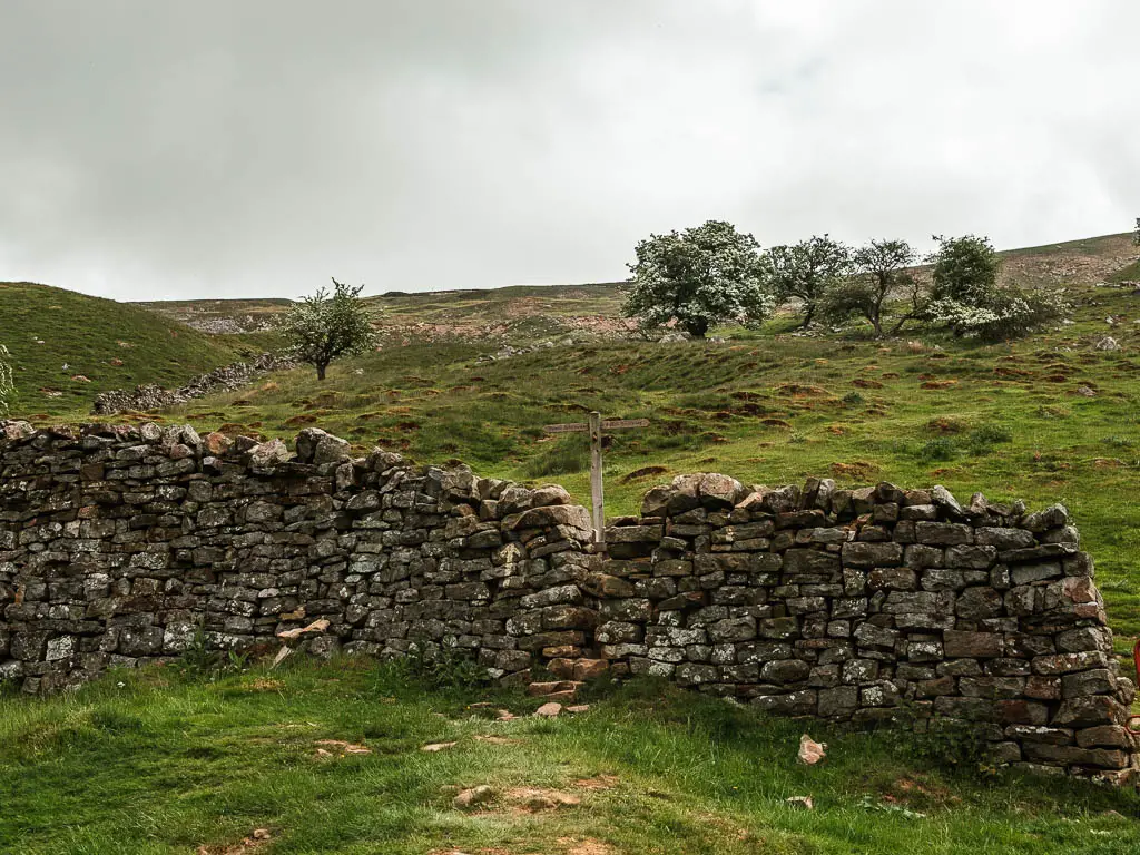 A rugged stone wall, with a wooden trail signpost on the other side, and a hill rising up behind.