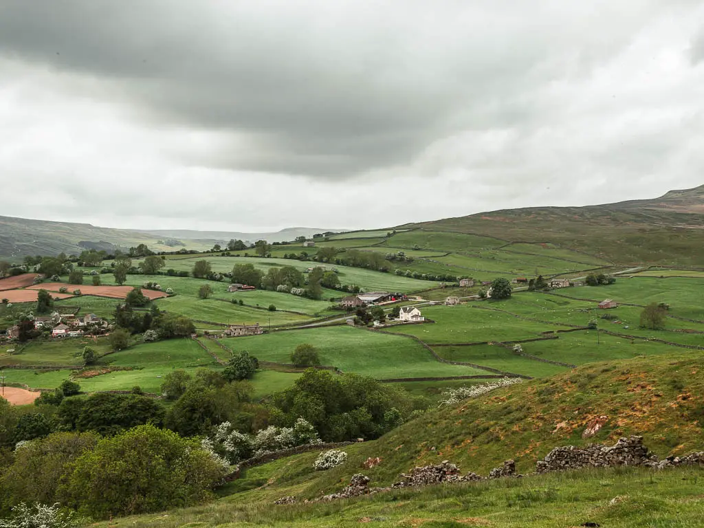 Looking down the hill into the valley of undulating green fields, when walking up to the top of Fremington Edge.