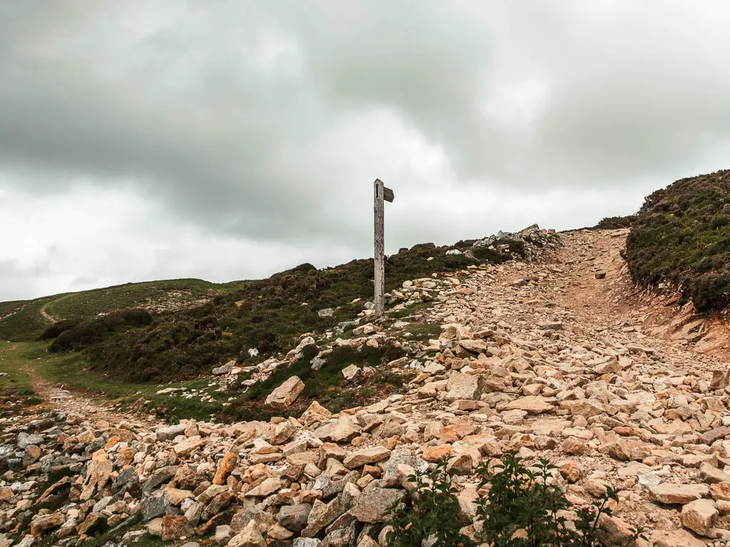 A rocky path junction, with a wooden trail signpost pointing straight ahead towards Fremington Edge.