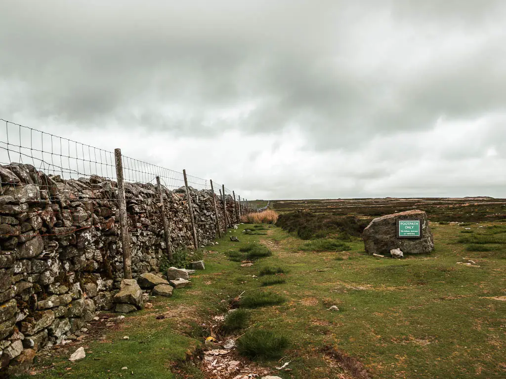 A stone wall with a wire fence on the left, running straight ahead across the moorland fields.